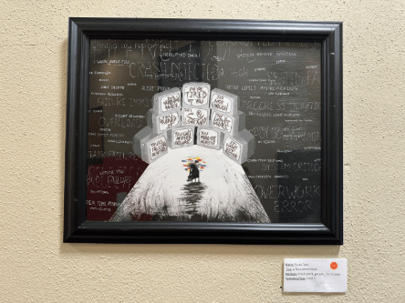 Framed mixed-media artwork titled “Hachiro” displayed on a gallery wall, featuring stacked illustrated cubes above a figure standing on a white hill against a dark background.