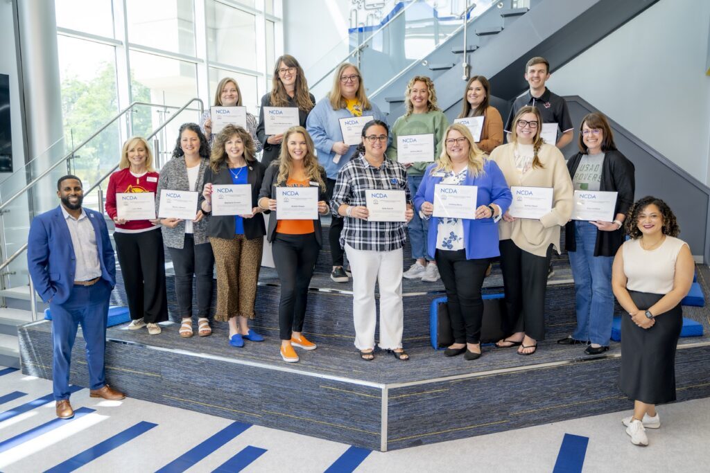 **Alt text:** Group of Rose State College employees stand on a staircase inside the Jeanie Webb Student Union holding National Career Development Association (NCDA) certificates after completing a professional development cohort program.