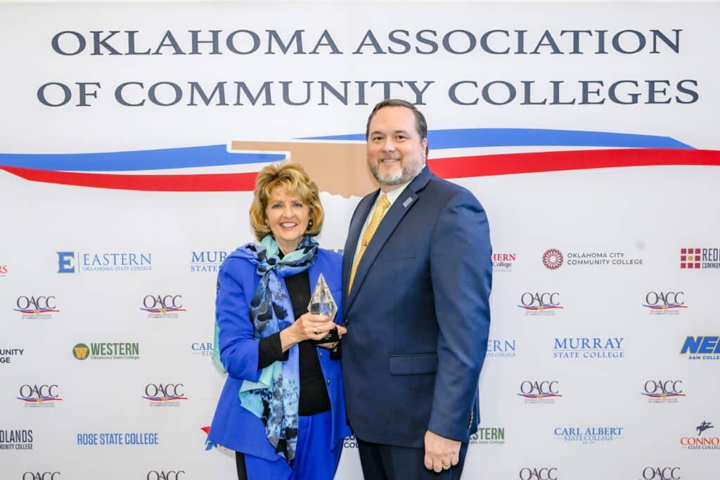 Dr. Jeanie Webb with President Travis Hurst smile in front of an OACC backdrop.
