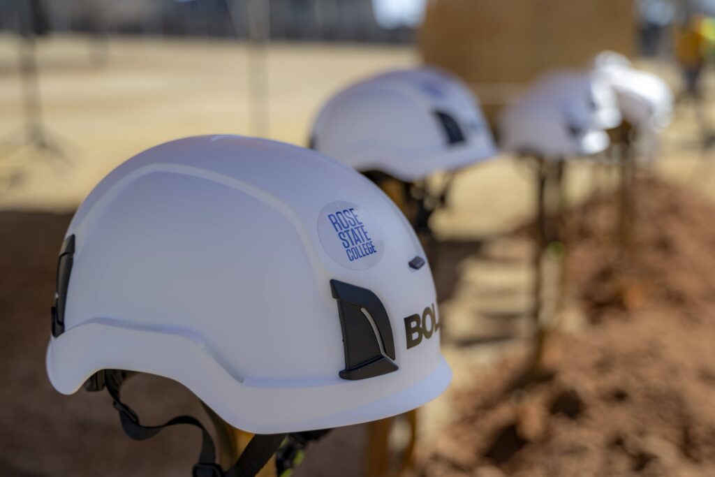 Rose State College hard hats lined up at a construction site during the Health Sciences groundbreaking ceremony.
