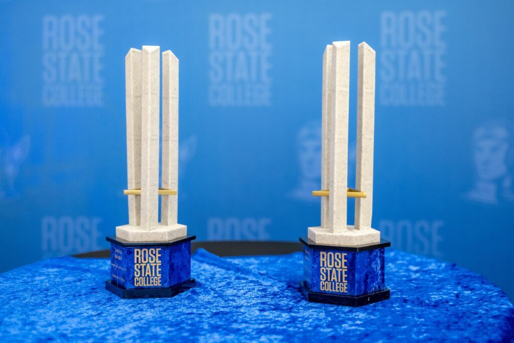 Two Rose State College Tower Awards displayed on a blue tablecloth in front of a Rose State College backdrop.