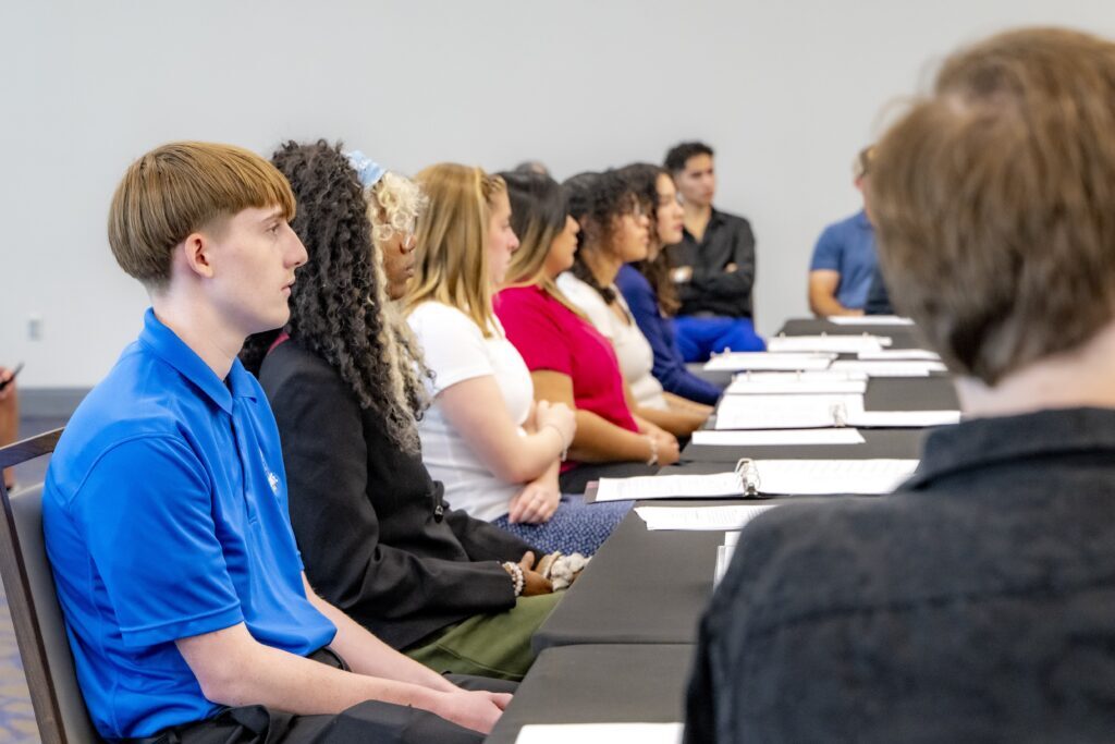 Rose State College Student Senate members sit at a conference table during a meeting, listening attentively with notebooks and binders open.