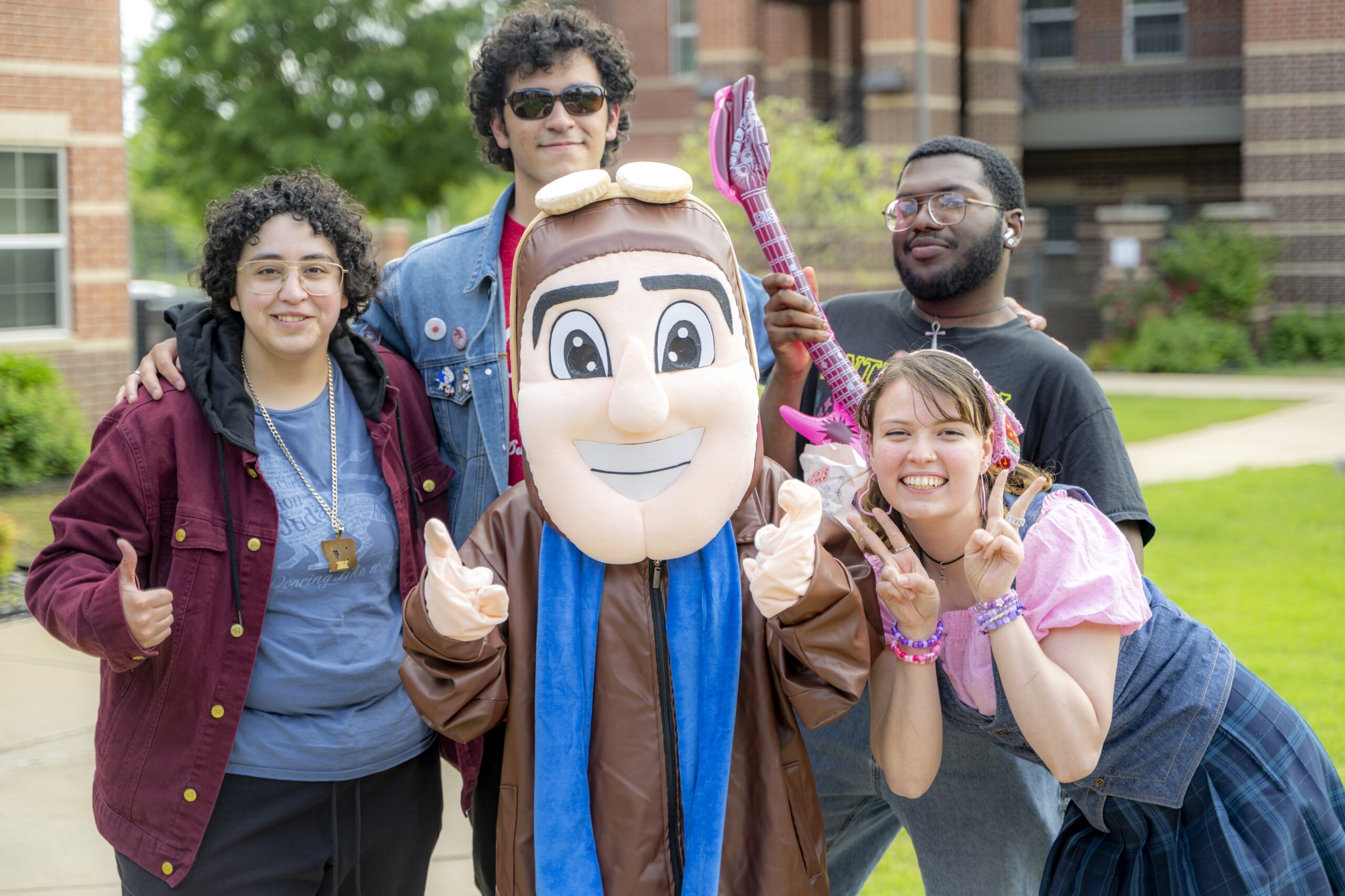 Four students pose outdoors with the Rose State College Raider mascot, smiling and making hand gestures during a campus carnival event.