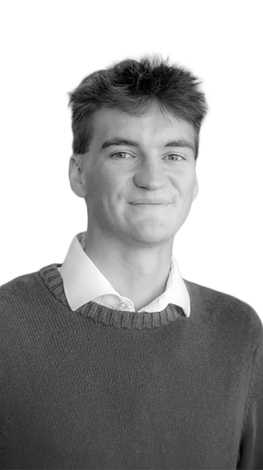 Head-and-shoulders portrait of a smiling Rose State College student wearing a white collared shirt and dark sweater, standing in front of a softly blurred wall.