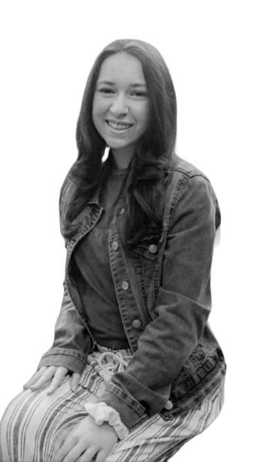 Black-and-white portrait of a smiling woman seated in a chair, wearing a denim jacket and striped pants, with long hair down.